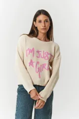 Sweater de punto color beige con diseño de texto en color rosa que dice 'I'm just a girl' y una estrella. Presenta cuello redondo, manga larga y corte holgado.