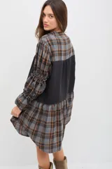 Vestido midi de corte holgado con diseño combinado en tela escocesa gris y naranja y panel central negro. Presenta cuello mao, cierre frontal con botones, mangas largas abullonadas con detalles de volados y puños elásticos.