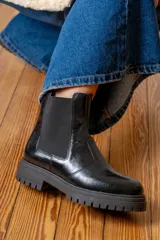 Bota tipo Chelsea de cuero negro con acabado brillante, paneles laterales elásticos y suela track dentada.