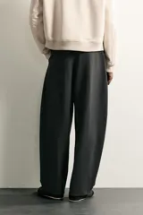 Pantalón de corte balloon fit en color gris oscuro, confeccionado en tejido con viscosa. Presenta pliegues frontales, cintura ajustable con cinturón integrado, bolsillos laterales y bolsillos traseros de doble vivo. Cierre frontal con cremallera y botón.