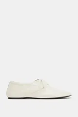 Zapatos planos de piel color blanco, con cierre de cordones en el empeine y detalle de pespuntes decorativos.
