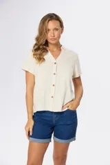 Camisa lisa de lino color beige, de manga corta, con cuello camisero, bolsillo ojal en el pecho y cierre frontal con botones.