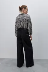 Jean wide leg negro de tiro alto, confeccionado en denim rígido, con diseño de cinco bolsillos, presillas para cinto, cierre frontal con botón y ruedo desflecado.