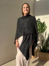 Ruana tejida en punto jersey, color negro con destellos brillantes de lurex. Presenta una etiqueta de cuero sintético con logo en la parte posterior.