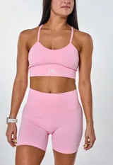 Conjunto deportivo de dos piezas color rosa, compuesto por un top de tirantes finos con logo estampado en el frente y un short de tiro alto con diseño sin costuras.