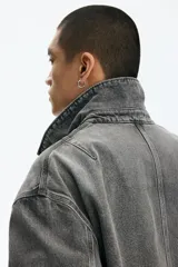 Campera de denim de algodón rígido, color gris oscuro con efecto gastado, cuello clásico, hombros caídos y cierre frontal. Cuenta con bolsillos delanteros ribeteados, un bolsillo superior con cierre y bajo recto.
