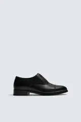 Zapato de vestir tipo Oxford en color negro, con diseño de puntera reforzada y cierre mediante cordones. Presenta una silueta clásica y elegante con tacón bajo.