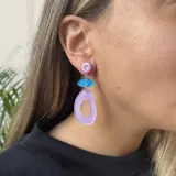 Aros colgantes con forma geométrica, con un botón rosa con un strass, una pieza celeste y una pieza lila con un agujero en el medio.