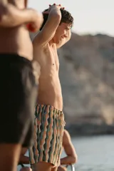 Short de baño con diseño de ondas verticales en tonos naranja, verde y beige. Cuenta con cintura elástica, dos bolsillos laterales y un bolsillo trasero con cierre.