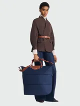 Bolso de viaje ampliable Longchamp modelo Le Pliage Original, color azul marino. Presenta diseño minimalista con asas cortas y correa larga ajustable en color marrón, cierre superior con solapa de cuero y botón a presión metálico.