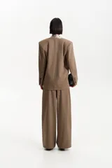 Blazer de color marrón topo, con un solo botón de cierre frontal y solapas anchas con forro interior en tono beige metalizado. Presenta bolsillos de solapa y un corte holgado.