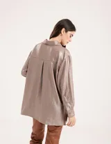 Camisa oversized con terminación metalizada color gris plomo. Tiene botones a tono en el delantero, largo por debajo de la cadera y tajos a los costados.