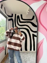 Buzo de corte holgado con diseño de rayas horizontales anchas en color chocolate y crudo. Presenta cuello redondo en color verde menta y puños elásticos.