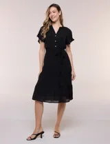 Vestido midi blanco de calce suelto y caída fluida, con escote en V, cuello a la base y apertura abotonada con detalle de puntilla. Cuenta con cintura elastizada con lazo para anudar a tono, mangas cortas con volados y falda con volantes escalonados.