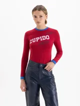 Remera de algodón pima con elastano, color rojo, de calce ajustado al cuerpo, manga larga y cuello redondo con detalles en color azul. Presenta estampa frontal con la palabra 'CUPIDO' y diseño de labios.