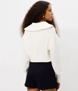 Campera cropped de tricot color blanco off-white, confeccionada en algodón con textura acanalada. Presenta cuello amplio con cierre metálico frontal, mangas largas con puños acanalados y cintura marcada con banda ancha.