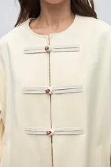 Capa de lana fina sin teñir, con diseño de corte amplio y mangas tipo kimono. Presenta cierre frontal mediante tres alamares de cuero en tono marrón.
