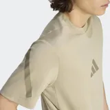 Remera Adidas de corte clásico y cuello redondo, color beige, con logo de la marca estampado en el centro del pecho y detalles gráficos en las mangas. Confeccionada en algodón fresco con protección UV.