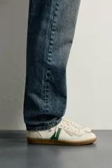 Zapatillas de estilo retro para hombre, color blanco off-white con detalles en verde oscuro y suela de goma marrón estilo gum. Presenta cordones al tono, refuerzos en gamuza en la puntera y talón, y bandas laterales verdes en contraste.