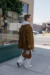 Chaqueta larga de piel color marrón, con cuello solapa, manga larga, bolsillos delanteros de plastrón y cierre frontal con botones.