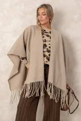 Ruana abierta de color beige, confeccionada en tejido de punto con terminación de flecos en el ruedo.