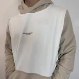 Canguro con capucha de diseño bicolor, combinando paneles en color blanco y beige. Presenta un bolsillo frontal tipo canguro y el logo de la marca bordado en el pecho.