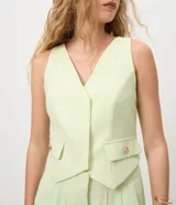 Chaleco de crepe color verde menta con escote en V profundo, sin mangas, bolsillos o falsas solapas con botones dorados y ruedo asimétrico en punta.