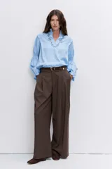 Blusa celeste de manga larga con puños fruncidos y elásticos, escote en V con cuello alto con volados y delicados bordados florales en el pecho.