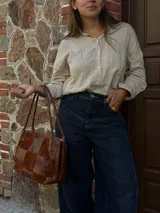 Cartera de hombro confeccionada en cuero y gamuza con diseño de damero, combinando paneles de texturas lisas y aterciopeladas. Presenta una manija trenzada y detalles de costuras artesanales en los laterales.