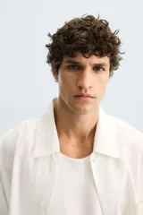 Camisa de corte relajado, color blanco hueso, con finas rayas verticales en tono grisáceo. Presenta cuello solapa, manga larga, bolsillo de parche en el pecho y bajo con aberturas laterales.