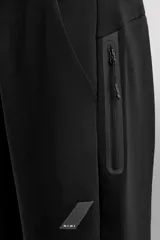 Pantalón jogger de entrenamiento, corte regular fit, color verde oliva oscuro. Confeccionado en tejido técnico compacto de algodón con elasticidad y efecto neopreno. Presenta cintura elástica ajustable con cordón blanco, bolsillos frontales y un bolsillo lateral con cierre de cremallera. El bajo termina en puño.