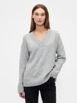 Buzo de punto en color gris melange, con escote en V y mangas largas. Presenta puños y ruedo acanalados, con un corte holgado y cómodo.