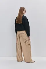 Pantalón cargo negro de corte relajado y pierna ancha con bolsillos laterales con solapa, cintura con doble broche y cierres metálicos en los tobillos.