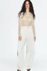 Top de manga larga confeccionado en tejido de encaje con diseño floral, de color blanco y corte recto con cuello redondo.