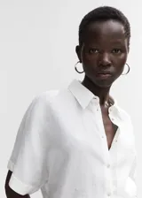 Camisa blanca de lino con cuello clásico, manga corta, corte oversize, cierre frontal con botones y bolsillo de parche en el pecho.