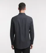 Camisa de manga larga confeccionada en tricolina de algodón, con cuello inglés, cierre frontal de botones y puños abotonados. Diseño liso y versátil.