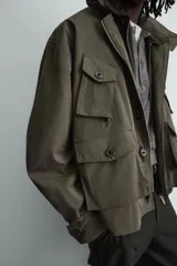 Cazadora relaxed fit de tejido con mezcla de algodón en color verde militar. Cuenta con cuello subido, manga larga con puño ajustable, múltiples bolsillos frontales de plastrón con solapa y cierre frontal con botones.