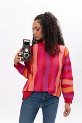 Buzo de tejido de punto con diseño de rayas verticales onduladas en tonos vibrantes como rojo, fucsia, naranja y rosa. Presenta cuello redondo, puños y ruedo acanalados, con un corte holgado y cómodo.