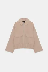 Cazadora beige de cuello solapa y manga larga, con bolsillos delanteros de plastrón con solapa, bajo elástico y cierre frontal con cremallera.