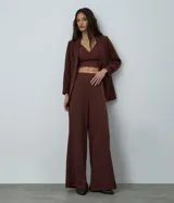 Pantalón de sastrería modelo pantalona, de corte amplio y tiro alto, con cintura lisa y pliegues frontales. Confeccionado en tejido de poliéster con elastano.
