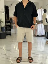 Camisa de lino color beige, de manga corta, con cuello abierto y cierre frontal de botones.