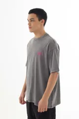 Remera gris con efecto acid wash, corte holgado y estampa pequeña en el pecho con diseño abstracto en color fucsia.