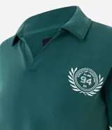 Saco deportivo de modal color verde, con cuello polo, escote en V y mangas largas con franjas blancas horizontales. Presenta un bordado circular en el pecho con la inscripción '94'.