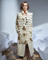 Tapado largo color natural de lana merino afieltrada, con cuello grande formado por piezas horizontales. Tiene bolsillos laterales y se puede usar suelto o cerrado con un accesorio.