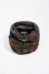 Mochila de estructura blanda confeccionada en nylon color marrón con estampado de cuadros tipo tartán. Presenta bolsillos laterales con cierre, solapa superior con bolsillo frontal y un detalle de cordón elástico en color verde neón.