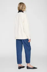 Chaqueta de corte relajado de algodón color blanco crudo, con cuello camisero a contraste en color negro, cierre frontal con cremallera, bolsillos aplicados y puños con botón, de inspiración utilitaria.