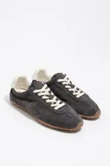 Zapatillas deportivas de perfil bajo confeccionadas en serraje color gris, con cordones claros y suela de goma con tachuelas características.