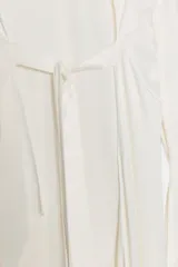 Top de viscosa con acabado satinado, cuello redondo y mangas largas acampanadas. Presenta un diseño de bajo asimétrico y cierre posterior con botones.