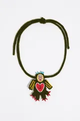 Collar artesanal de crochet en color verde militar con un dije en forma de figura bordada. El diseño incluye un corazón rojo en el centro, detalles amarillos y cuentas de vidrio celestes y rojas. Cuenta con un cordón tejido ajustable mediante un nudo.