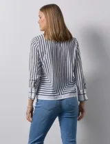Blusa de gasa estampada con líneas verticales negras sobre fondo beige, de manga larga con puño abotonado. Espalda con abertura y botón.